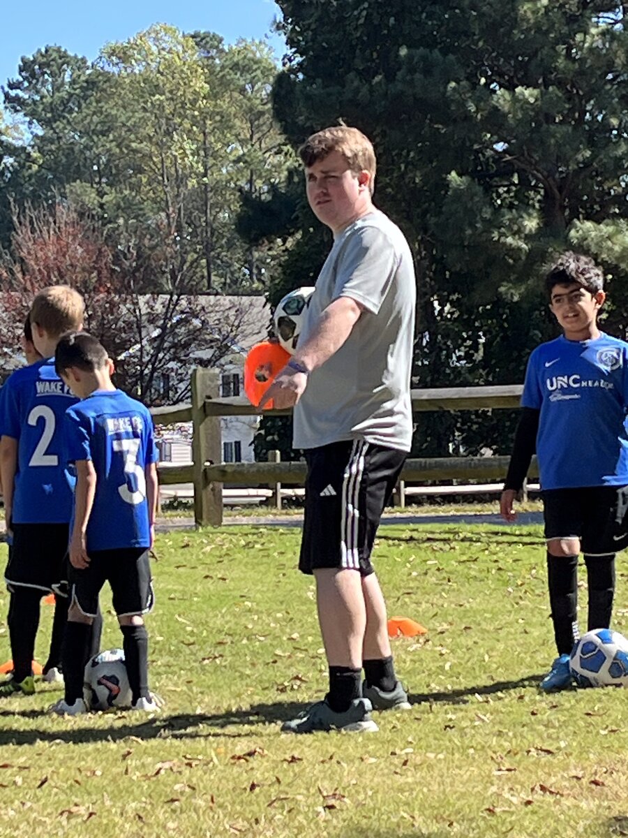 Coach Will holding a ball with Wake FC players
